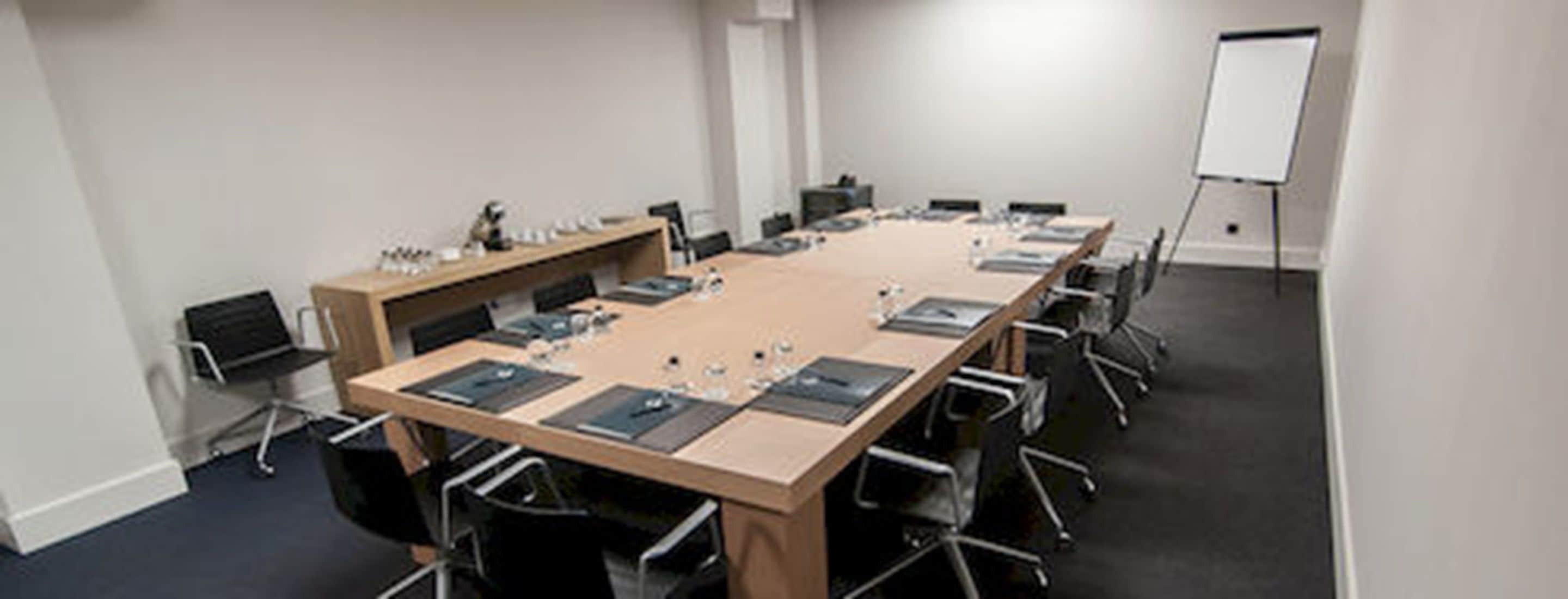 Een vergaderruimte met een lange tafel, stoelen, een whiteboard en een beamer.