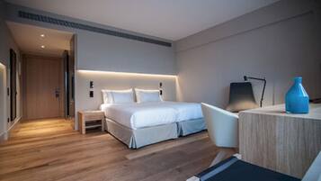Une chambre d’hôtel moderne avec un plancher en bois, un lit avec une literie blanche, un bureau avec une chaise et un vase bleu posé sur le bureau.