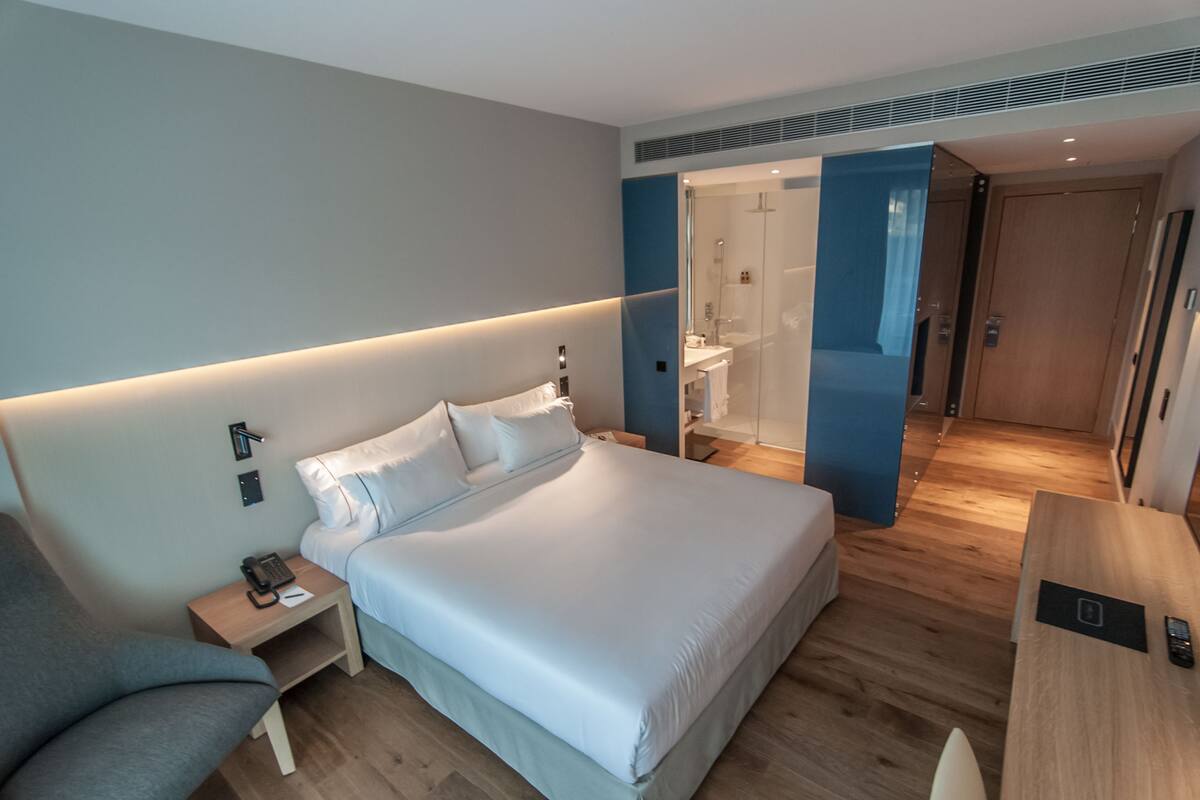 A modern hotel room with a large bed, bedside tables, a desk, and a shower area.