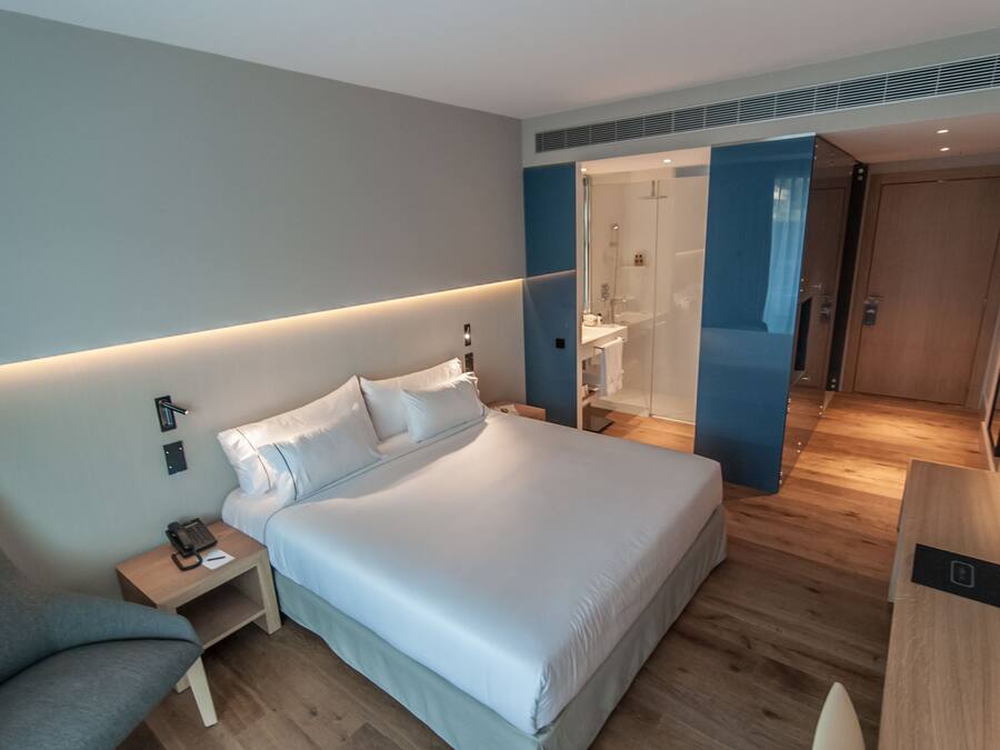 Una habitación de hotel moderna con una cama grande, mesitas de noche, un escritorio y un área de ducha.