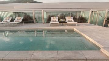 Piscina com espreguiçadeiras e vista para um edifício com grandes janelas.
