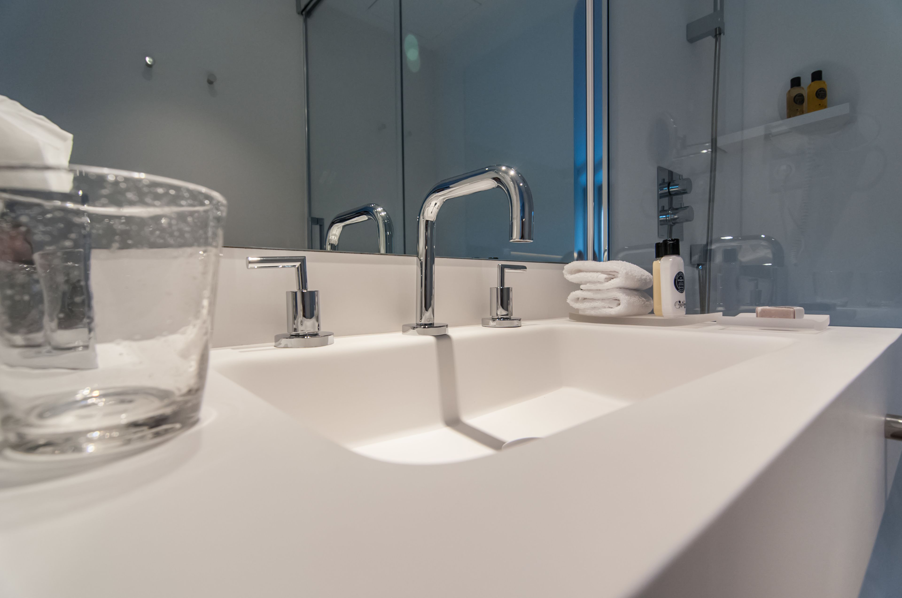 Un baño moderno con un lavamanos blanco, tres grifos cromados y un cuenco de vidrio sobre la encimera.