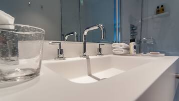 Un baño moderno con un lavamanos blanco, tres grifos cromados y un cuenco de vidrio sobre la encimera.