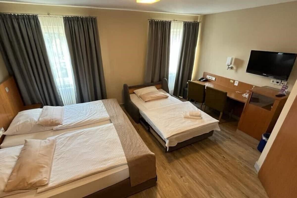 Een hotelkamer met twee éénpersoonsbedden, een bureau met een stoel, een televisietoestel en een raam met gordijnen.