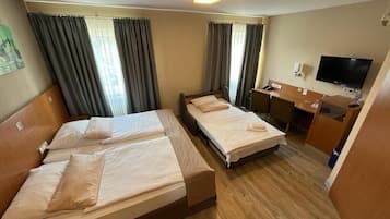 Habitació d'hotel amb dos llits individuals, una taula de treball amb cadira, televisió i finestra amb cortines.