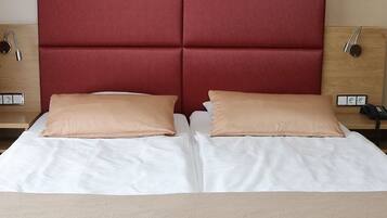 Una cama doble con dos almohadas color beige, un cabecero rojo, mesitas de noche con lámparas y un armario de madera.