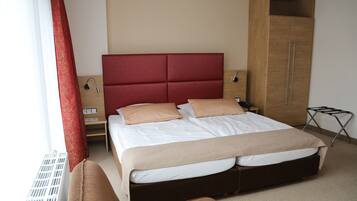A neatly made bed with a red headboard, a wooden wardrobe, and a small bedside table with a lamp.