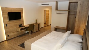 A modern hotel room with a large bed, a desk with a chair, a TV mounted on the wall, and a wardrobe.