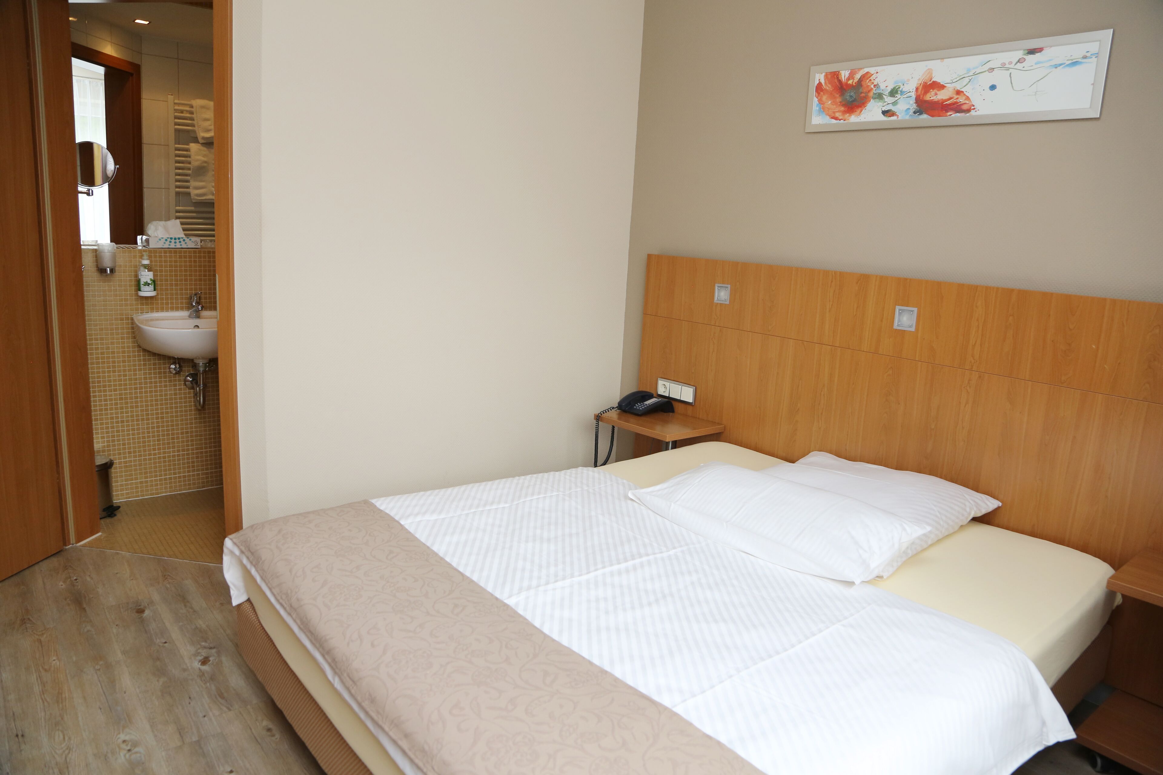 Una habitación de hotel con cama, mesita de noche y teléfono instalado en la pared.