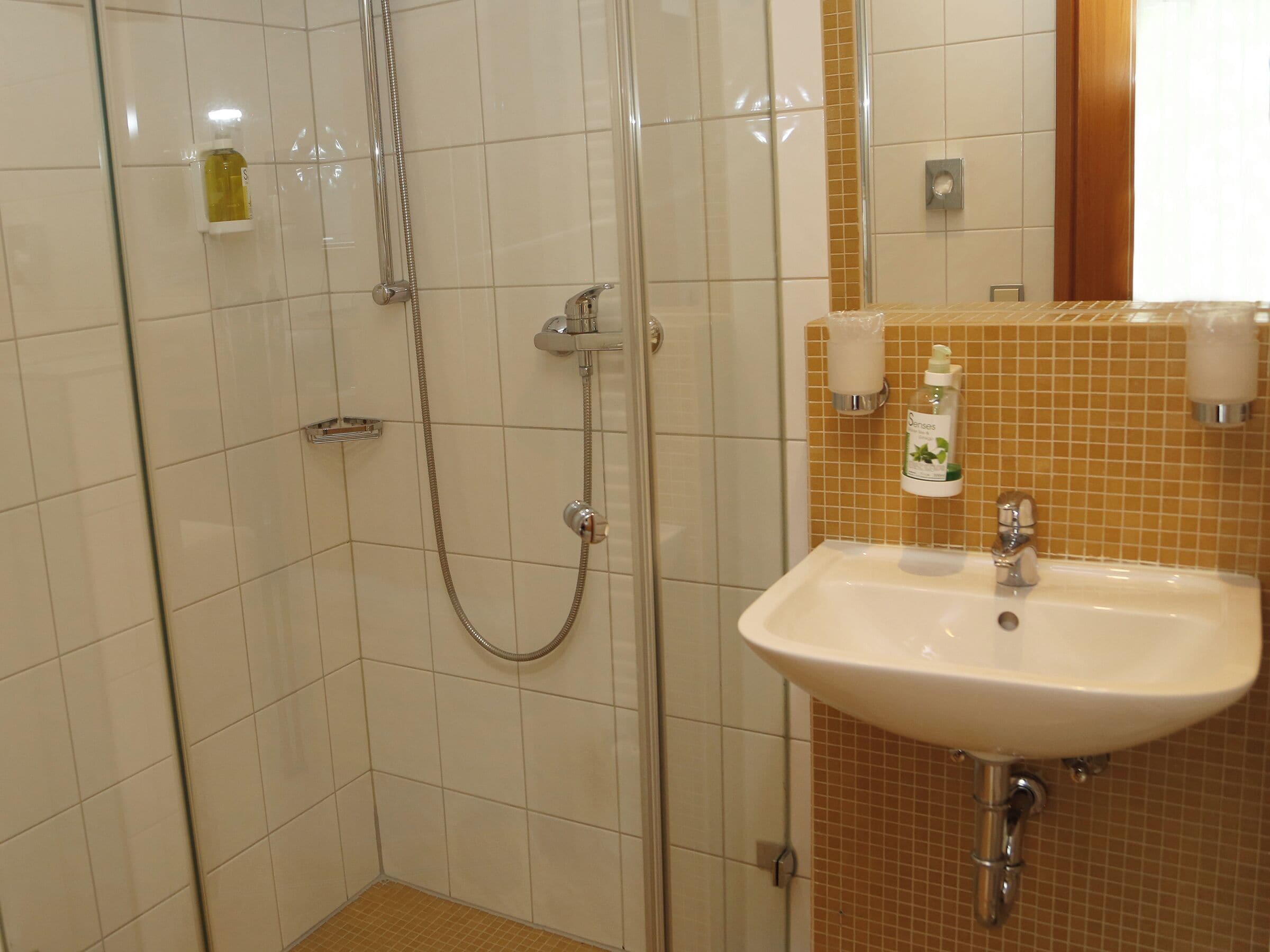 Un baño con ducha de vidrio, lavamanos blanco y artículos de tocador en la pared.