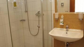 Un baño con ducha de vidrio, lavamanos blanco y artículos de tocador en la pared.