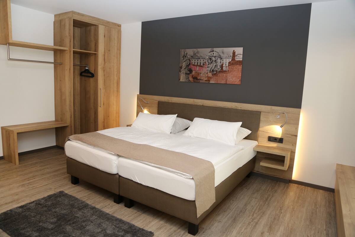 Een moderne slaapkamer met een groot bed, een houten garderobe, nachtkastjes en een wandlamp.