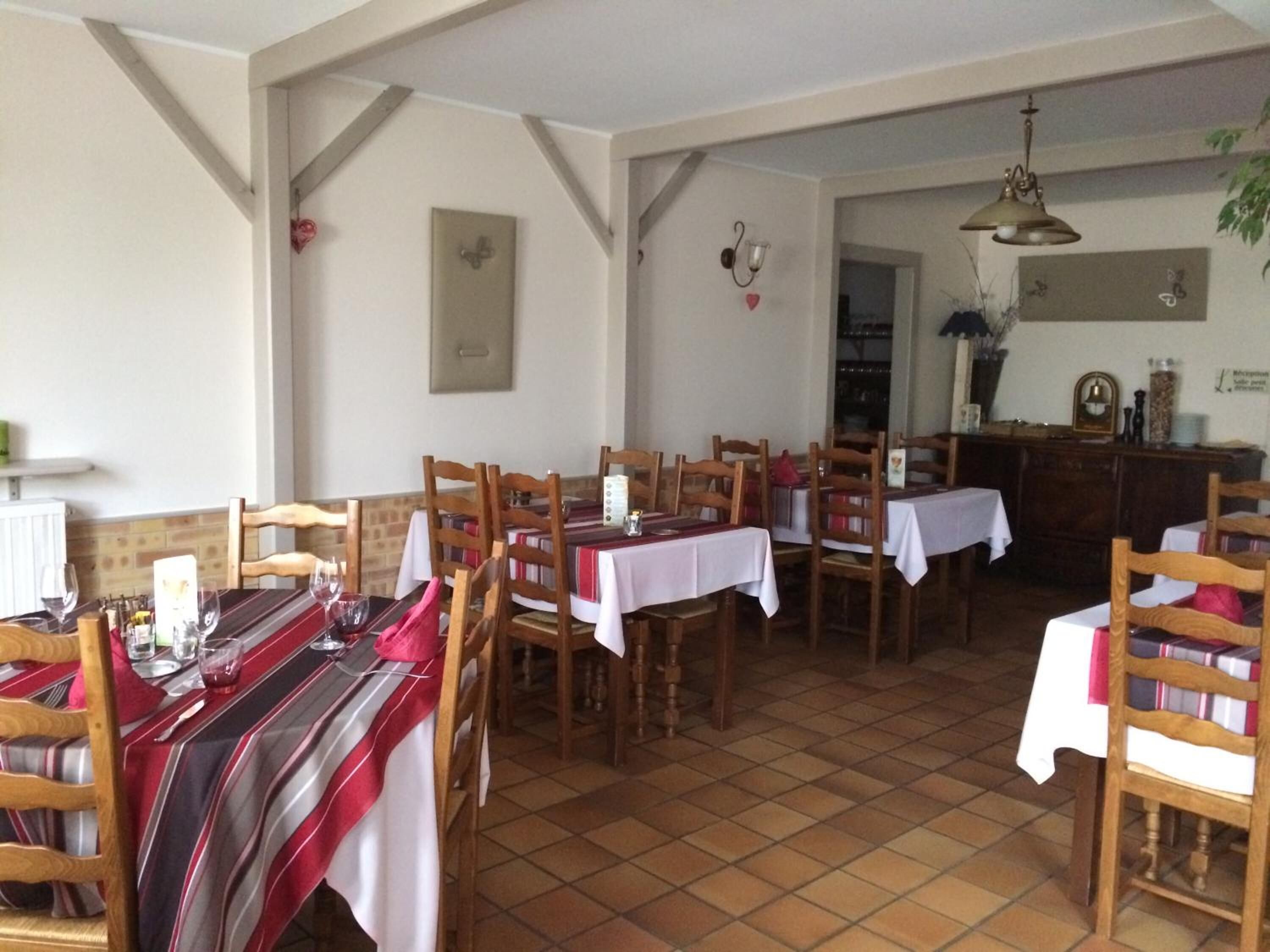 Un comedor con mesas y sillas de madera, manteles blancos y piso de baldosas.