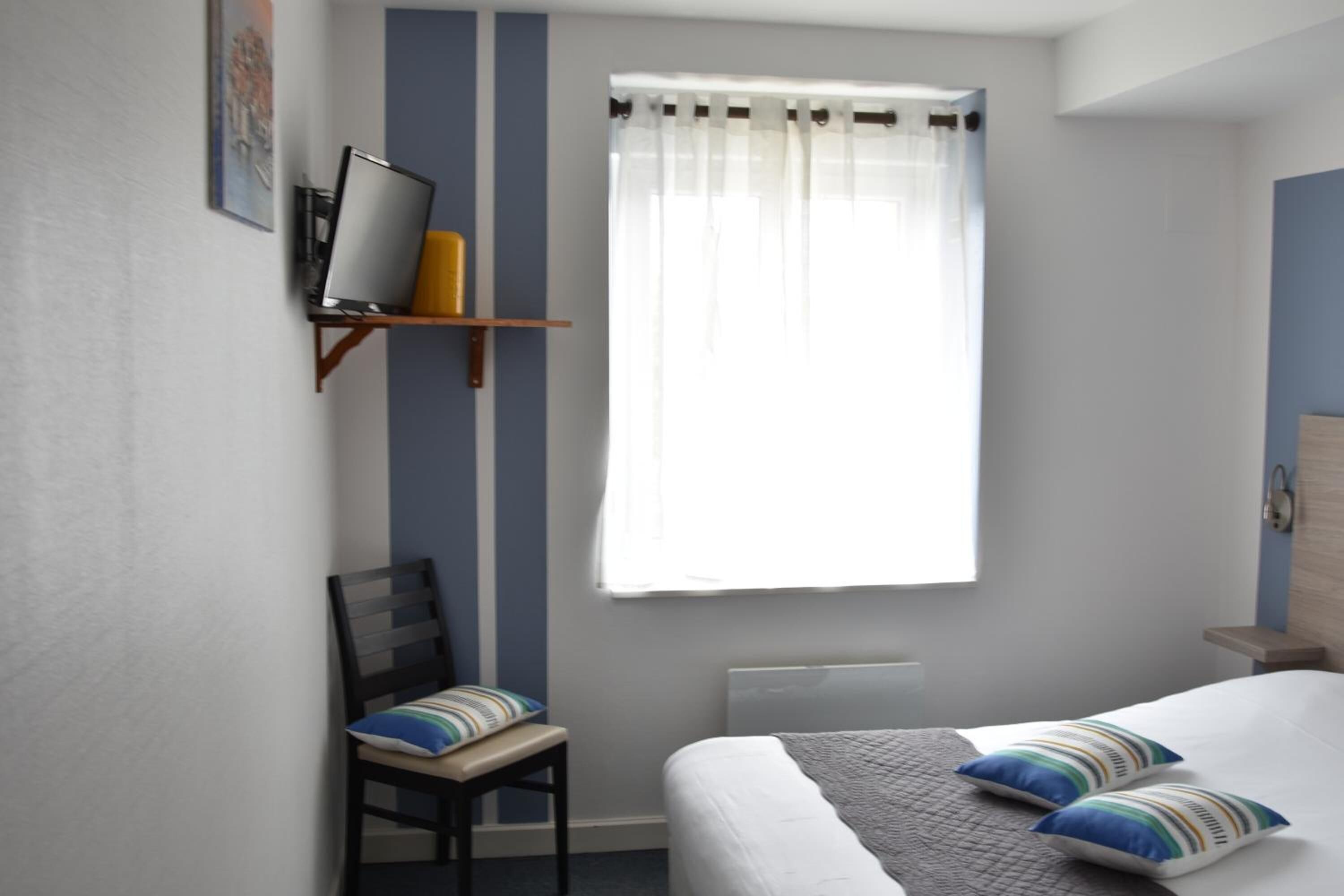 Ein Schlafzimmer mit einem Bett, einem Sessel, einem Schreibtisch und einem Fenster mit Vorhängen.