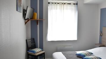 Ein Schlafzimmer mit einem Bett, einem Sessel, einem Schreibtisch und einem Fenster mit Vorhängen.