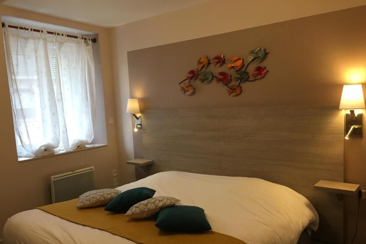 Un lit bien fait, recouvert d’un plaid blanc et moutarde, avec deux coussins turquoise et une œuvre d’art décorative accrochée au mur au-dessus.