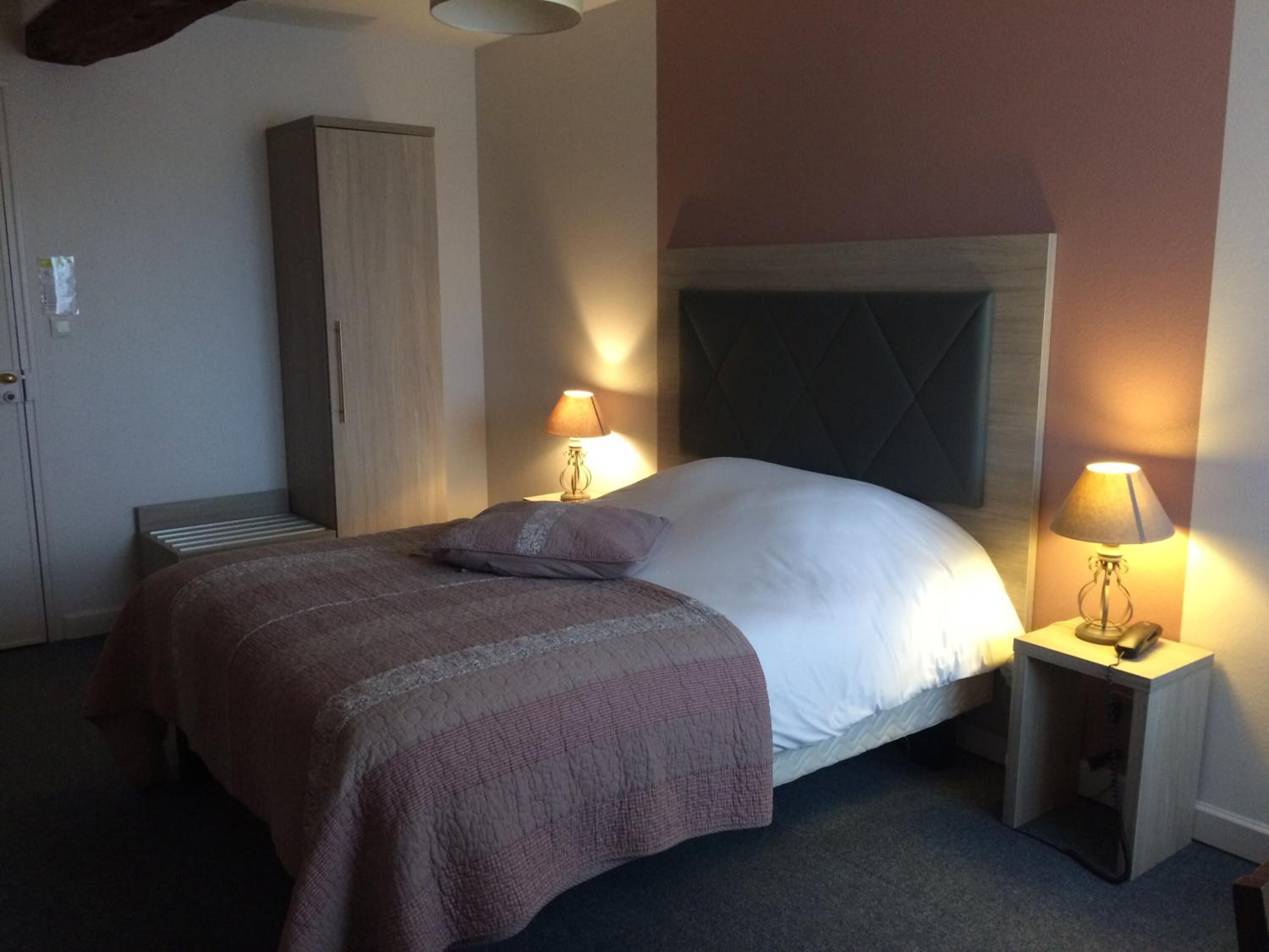 A hotel room with a bed, two bedside lamps, a wardrobe, and a carpeted floor.
