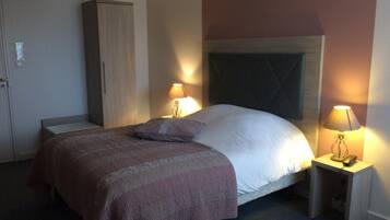 A hotel room with a bed, two bedside lamps, a wardrobe, and a carpeted floor.
