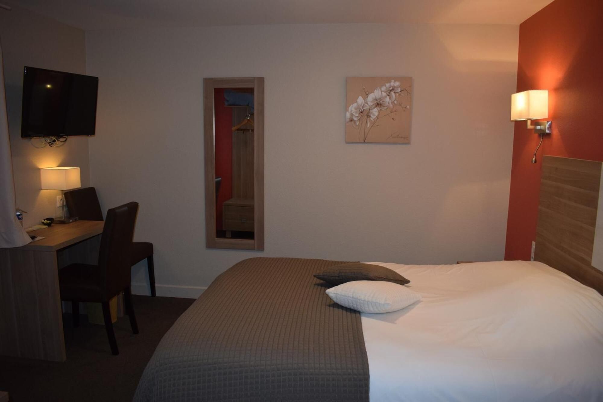 A hotel room with a bed, a desk with a chair, a TV mounted on the wall, and a painting on the wall.