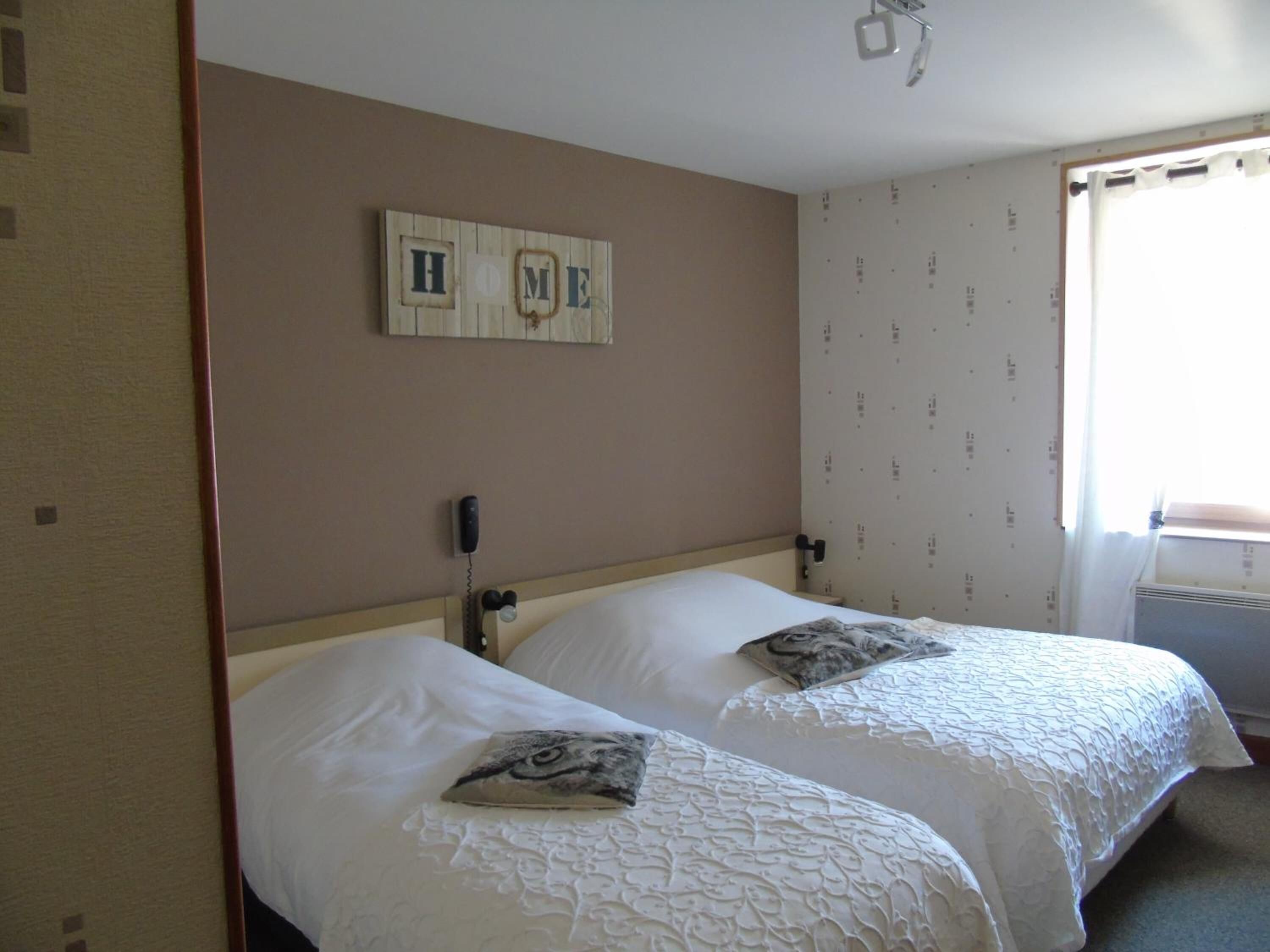 A hotel room with two beds, a wooden headboard, a wall-mounted phone, and a 'HOME' sign above the beds.