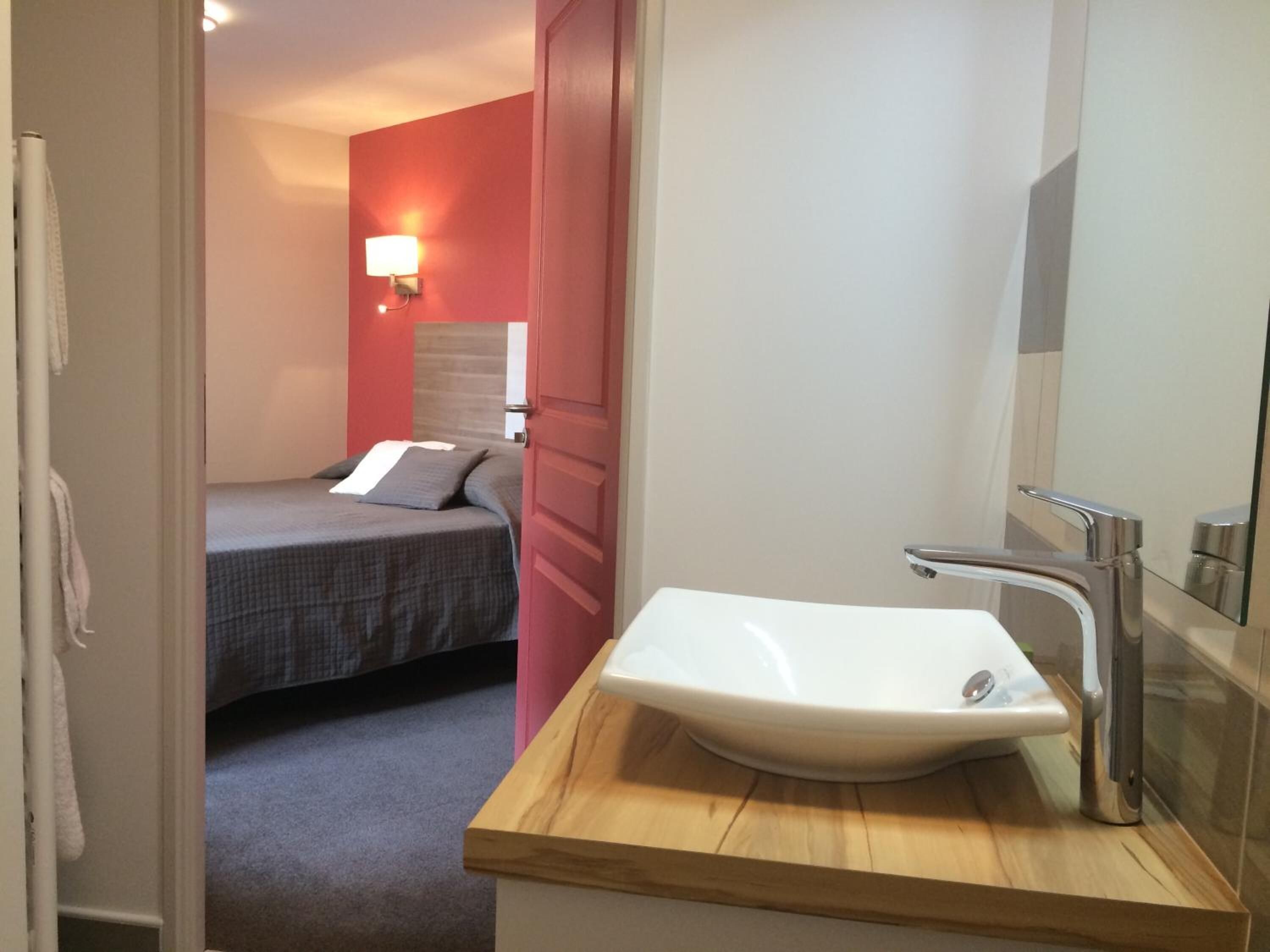 Une chambre d’hôtel avec un lit, une coiffeuse en bois dotée d’un lavabo et un mur d’accent de couleur rouge.