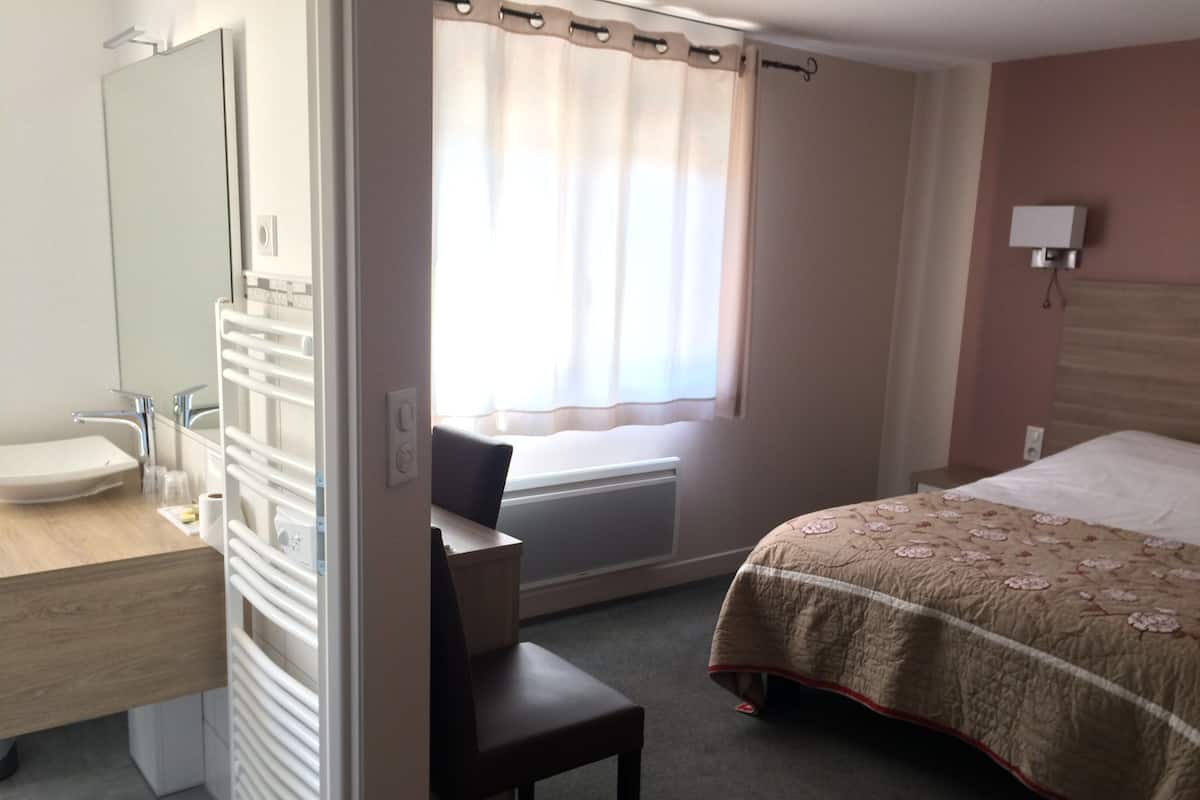 A hotel room with a bathroom, a bed, a desk, and a chair.