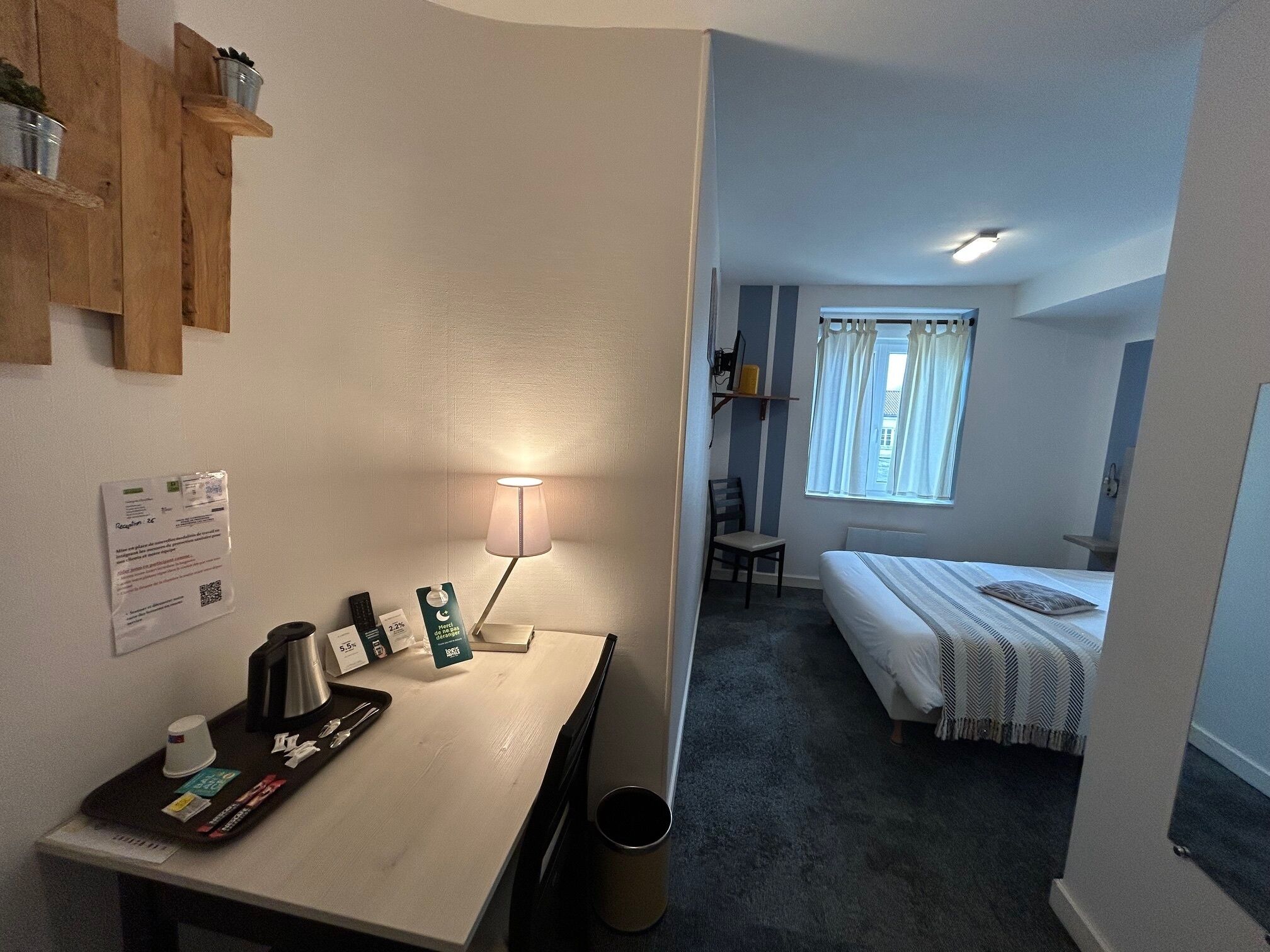 Habitación de hotel con escritorio, lámpara, cama y ventana con cortinas.