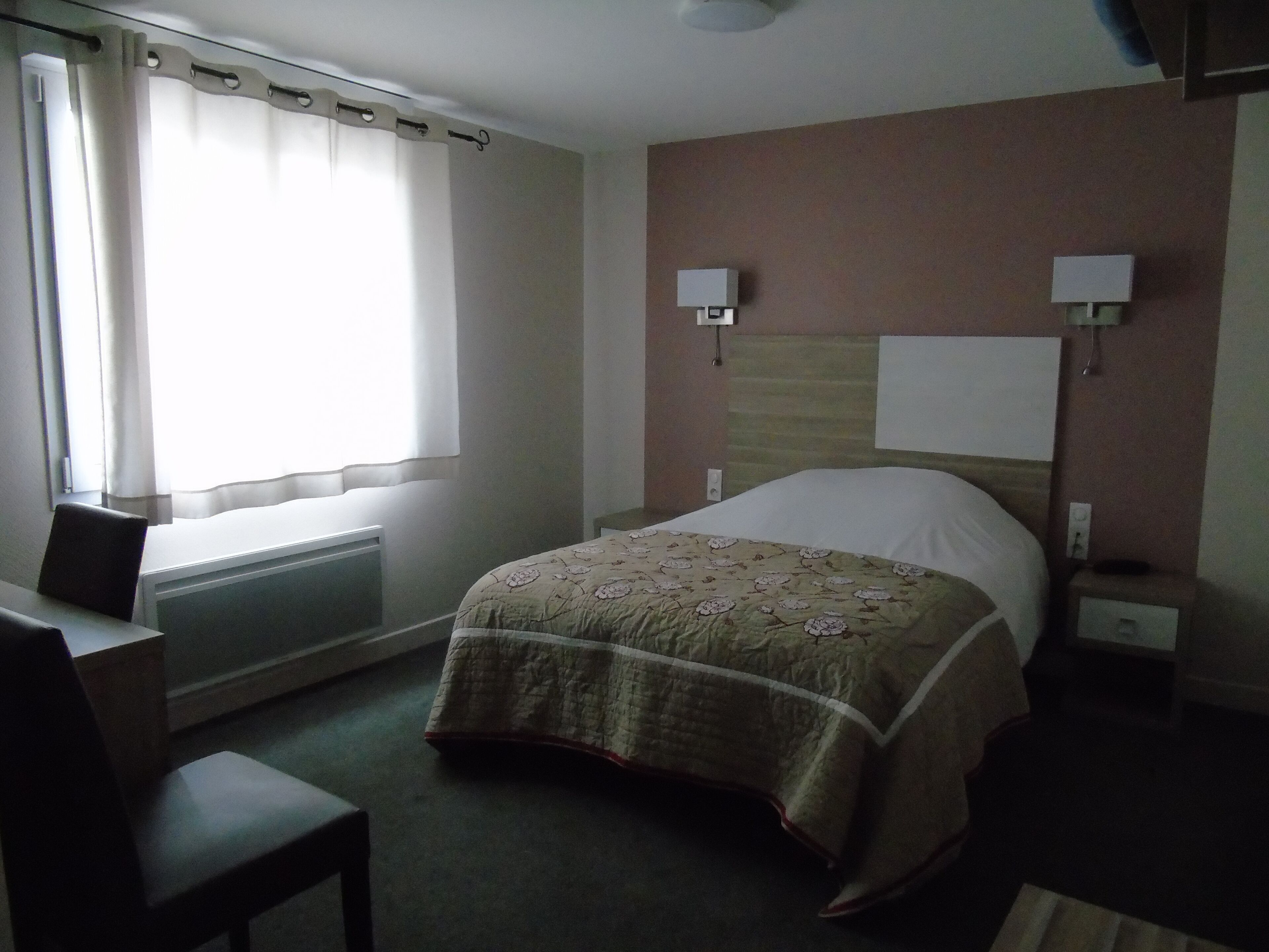 Una habitación de hotel con cama, escritorio, silla y ventana con cortinas.