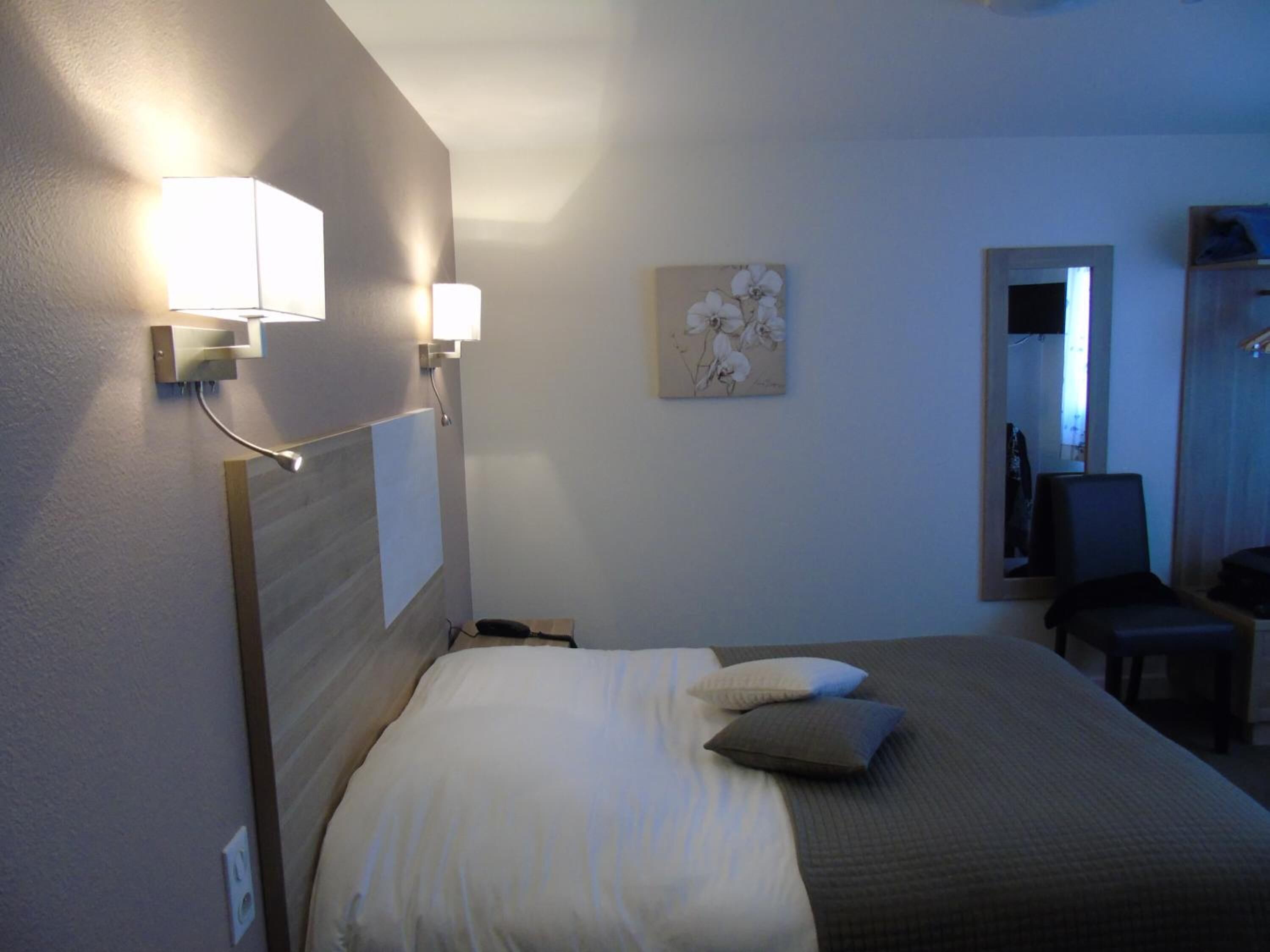 Una habitación de hotel con una cama, lámparas de noche, un cuadro, una silla y un escritorio.
