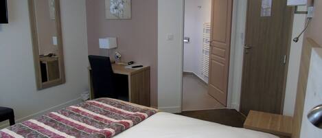 A hotel room with a bed, a desk, a chair, a mirror, and a door leading to another room.