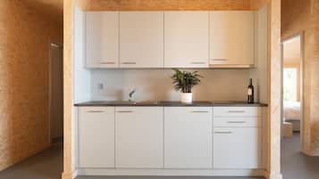 Une cuisine moderne avec des meubles blancs, un plan de travail, un évier, une plante en pot et une bouteille de vin.