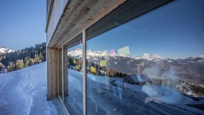 Un edificio moderno con un gran ventanal que refleja un paisaje montañoso nevado.