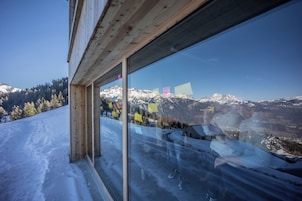 Un bâtiment moderne doté d’une grande fenêtre en verre qui reflète un paysage montagneux enneigé.