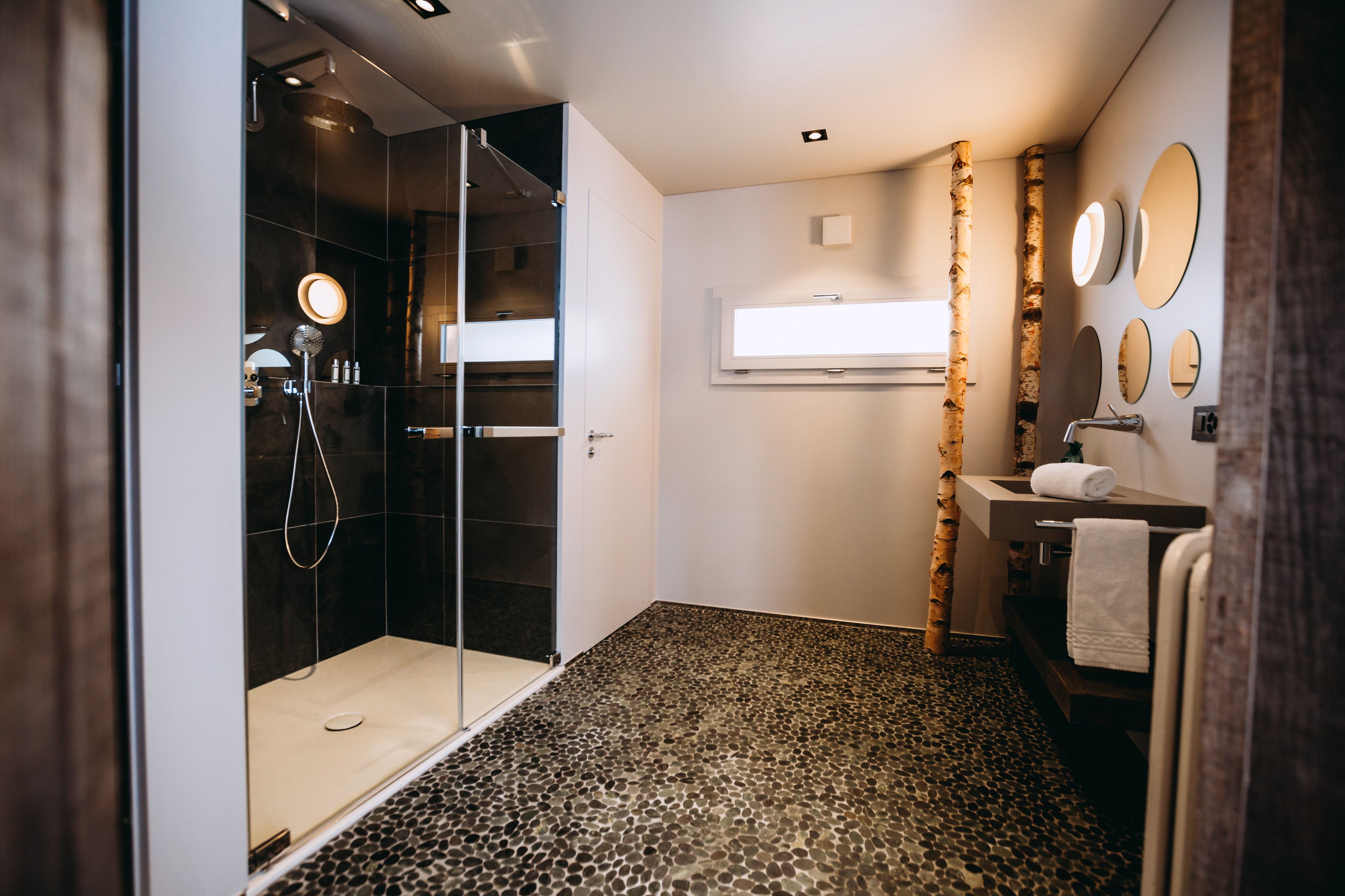 A modern bathroom with a glass-enclosed shower, a vanity with a mirror, and a textured floor.