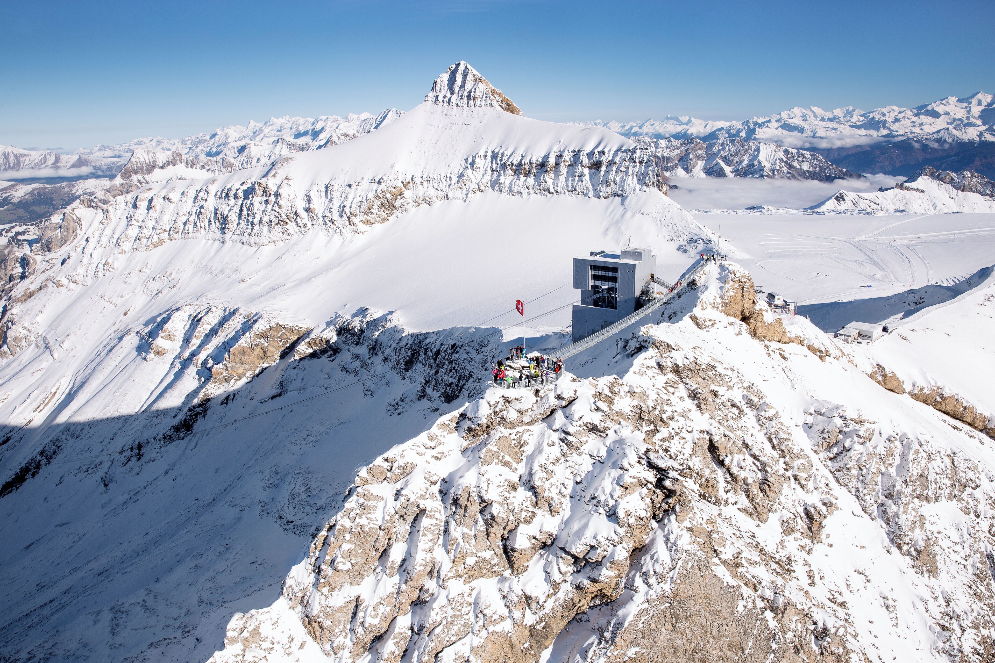 Una montaña nevada con un pequeño edificio en una cresta.