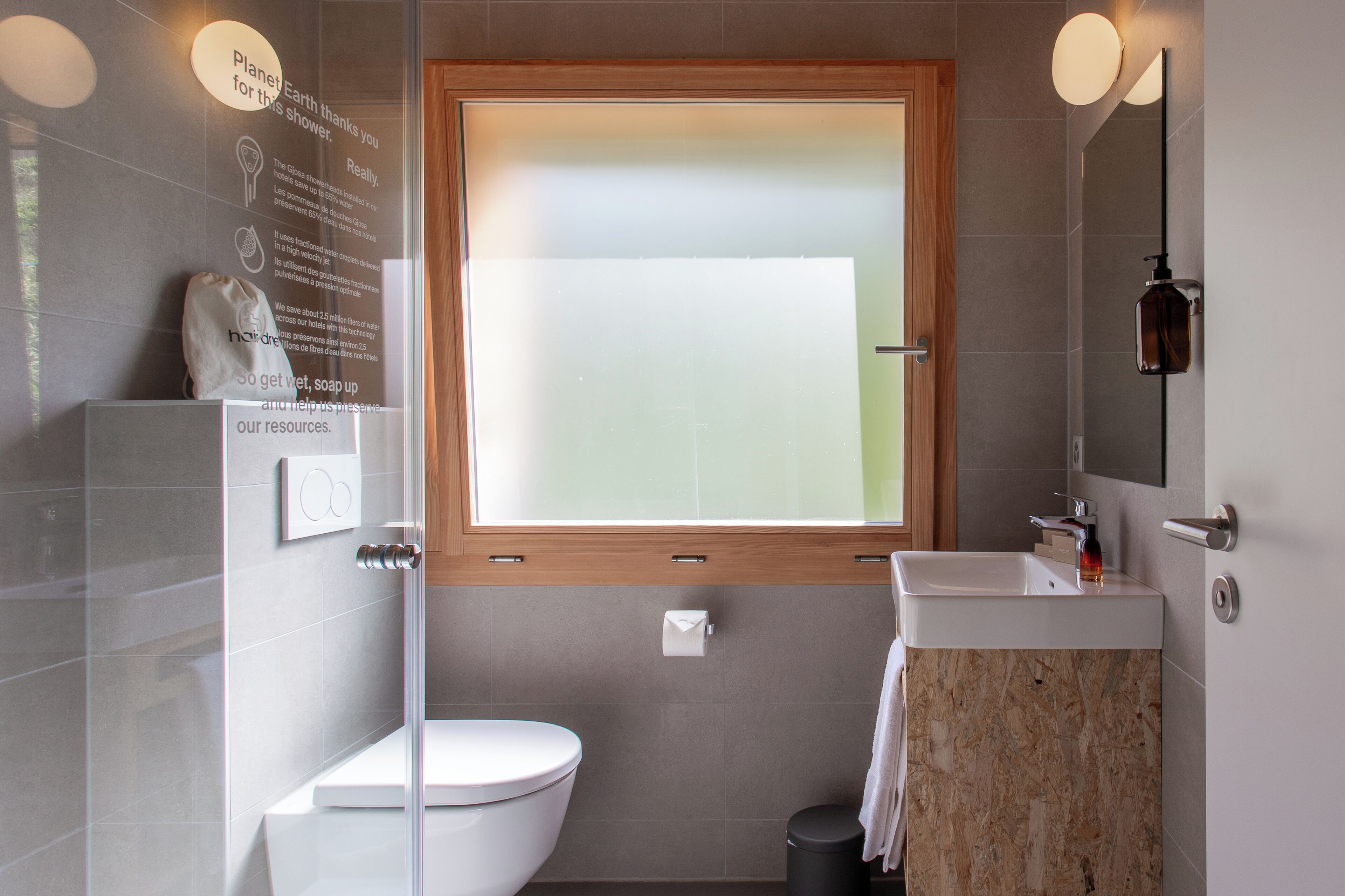 Un baño moderno con cabina de ducha de vidrio, inodoro blanco, lavabo con encimera de mármol y ventana con marco de madera.