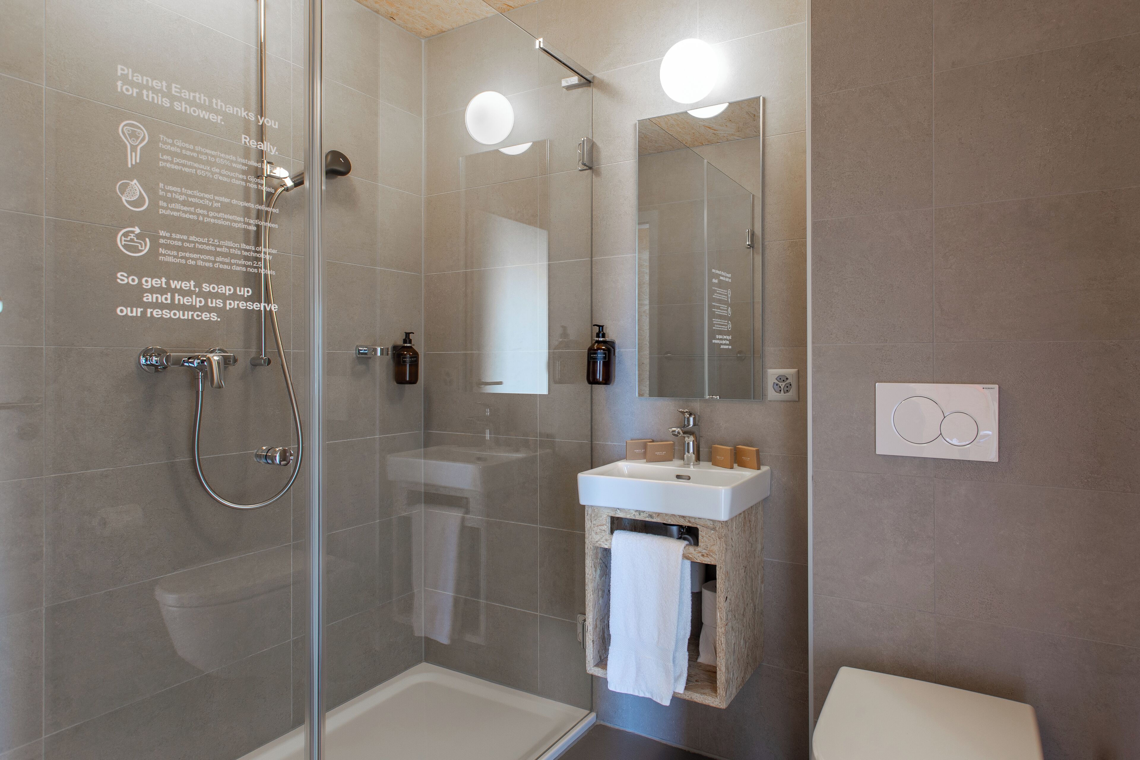 Een moderne badkamer met een douchecabine van glas, een wit wastafel en een houten wastafelmeubel.