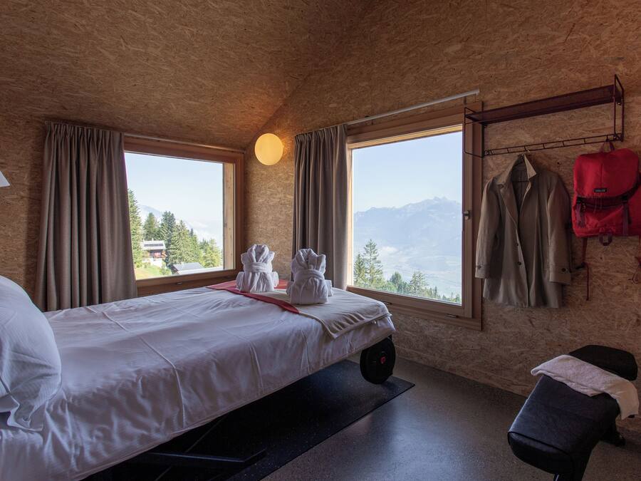 Una habitación con una cama, un banco y vistas a las montañas.