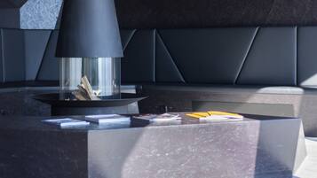 A modern interior with a central black conical structure, possibly a fireplace, surrounded by geometric seating and pendant lighting.