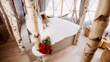 A room with birch tree pillars, a bed with white linens, and a small table with a bouquet of red roses.