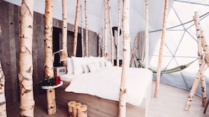Un dormitorio con troncos de abedul como muebles, una cama con ropa de cama blanca y una hamaca.