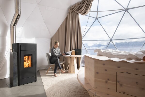 Una habitación moderna con estufa de leña, un ventanal con vistas a montañas y una zona de estar acogedora.