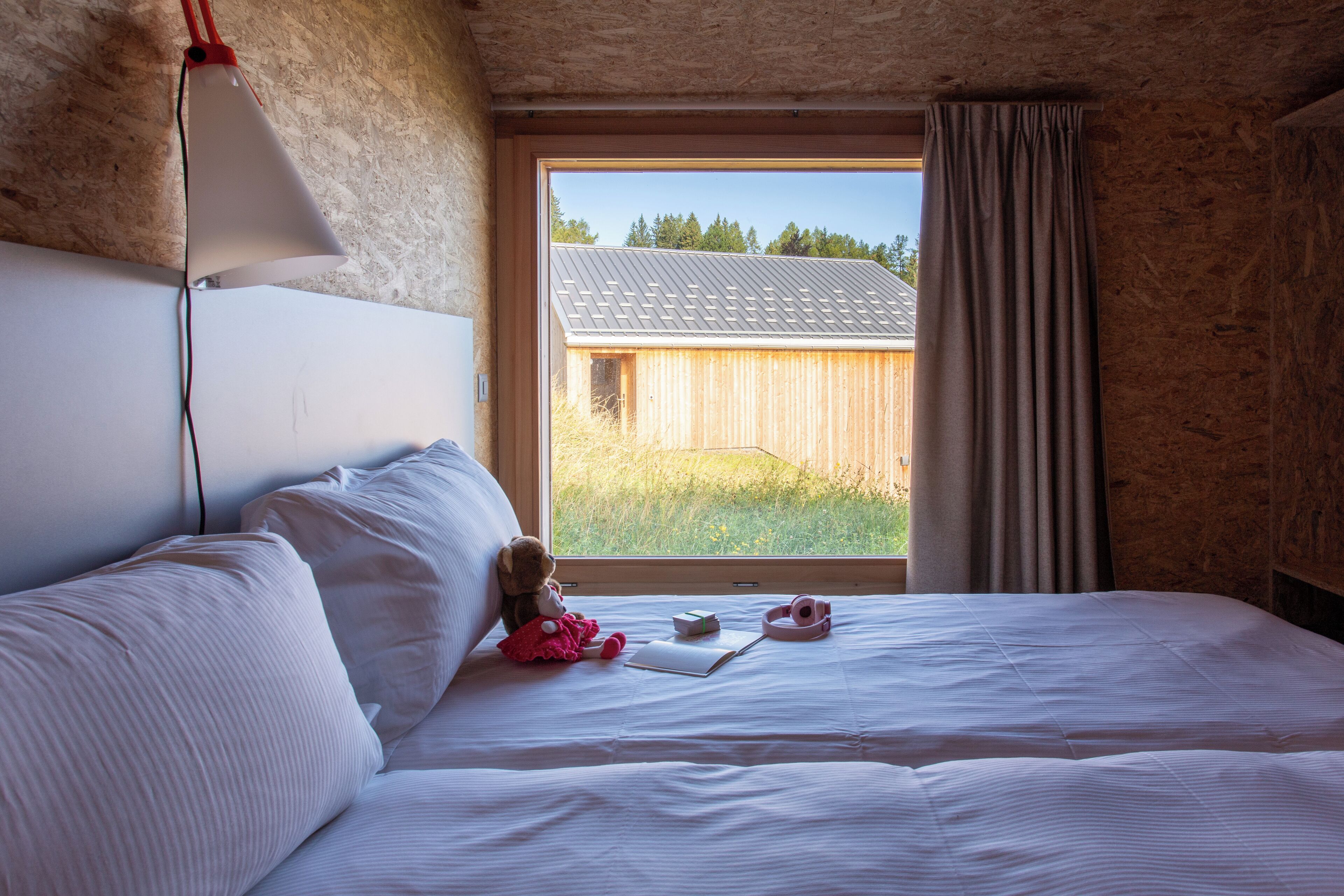 A bedroom with a large window, a bed, a teddy bear, and a lamp.