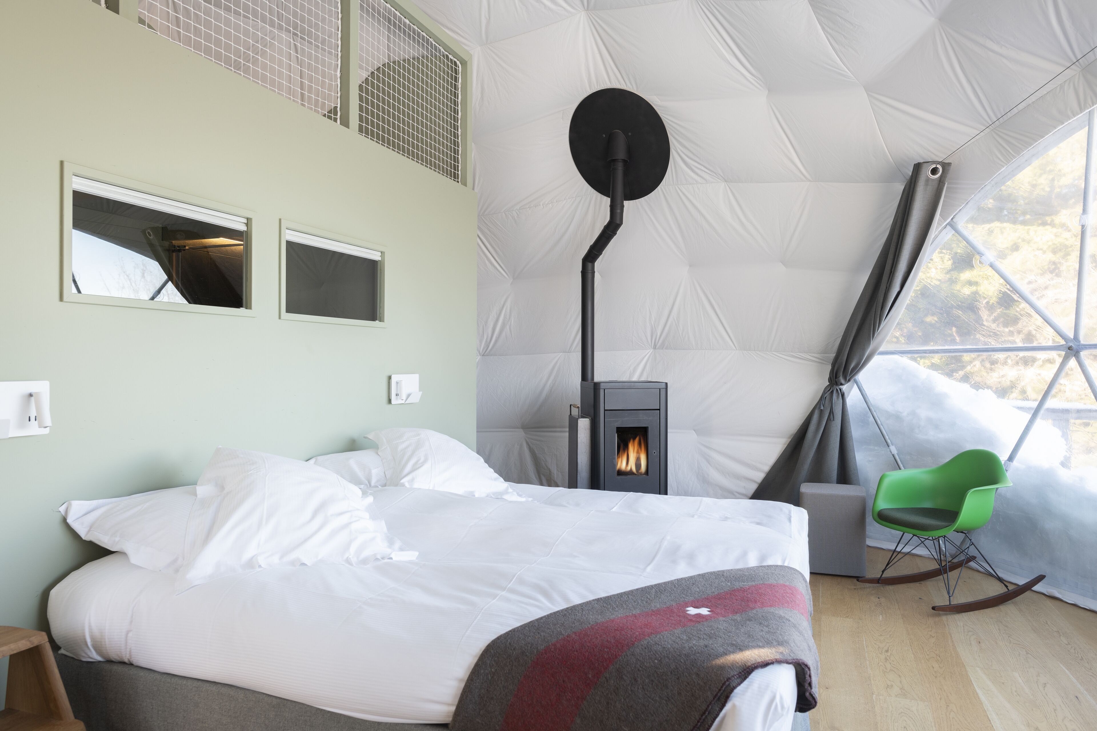 Una habitación acogedora con una cama, una chimenea, un sillón verde y una ventana.