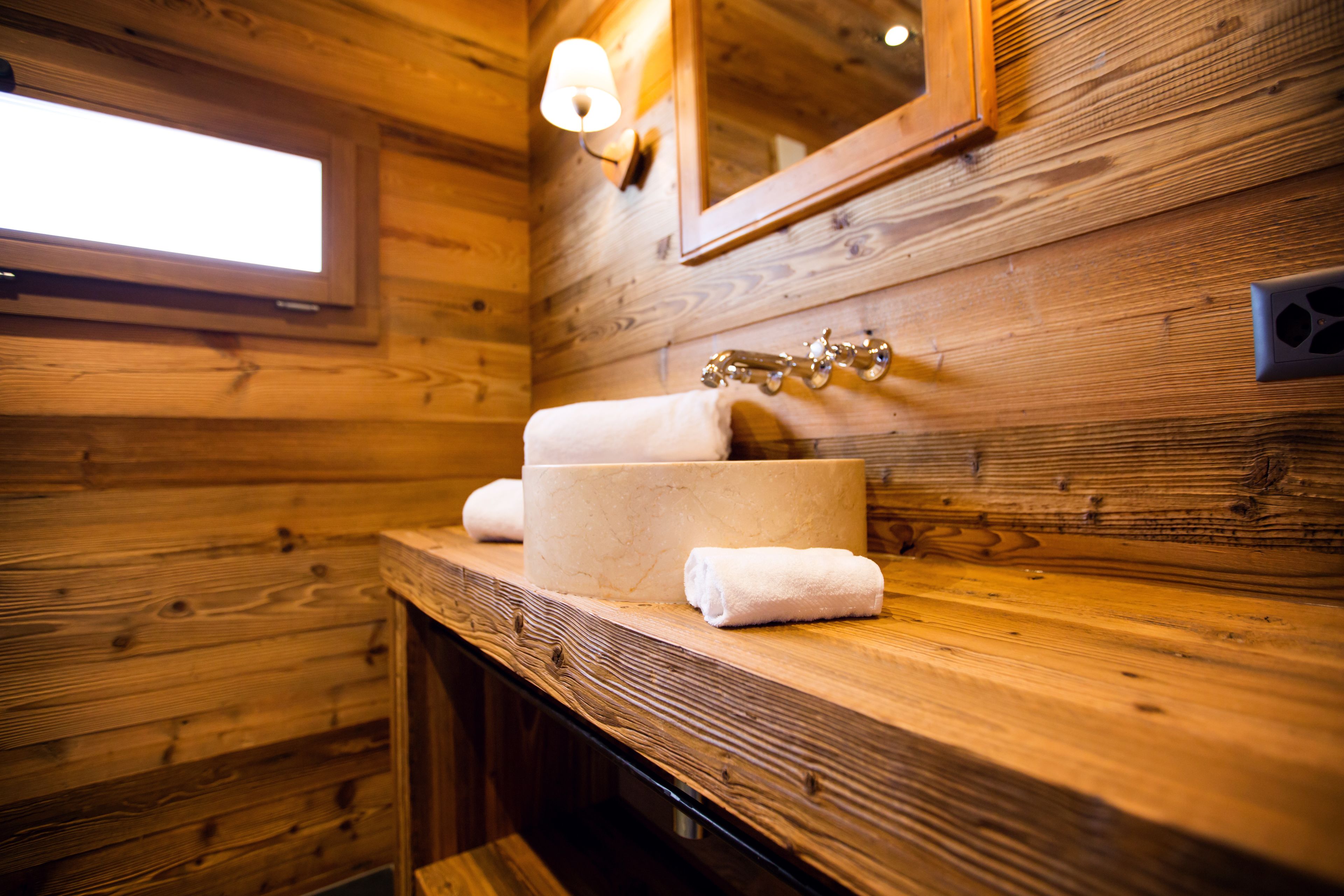 A wooden cabin bathroom with a sink, mirror, and window.