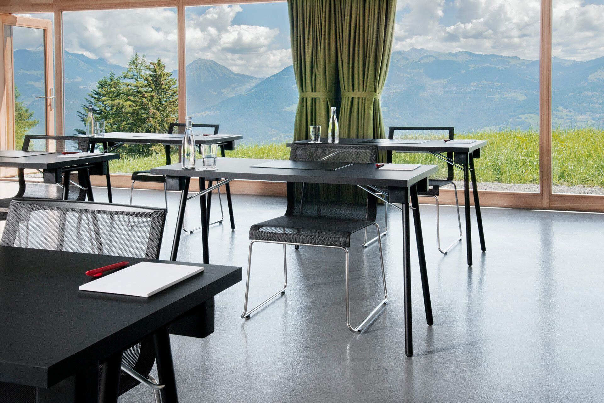 A modern dining area with tables and chairs, large windows with a mountain view, and a green curtain.