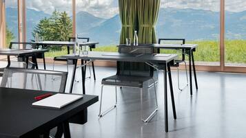 A modern dining area with tables and chairs, large windows with a mountain view, and a green curtain.