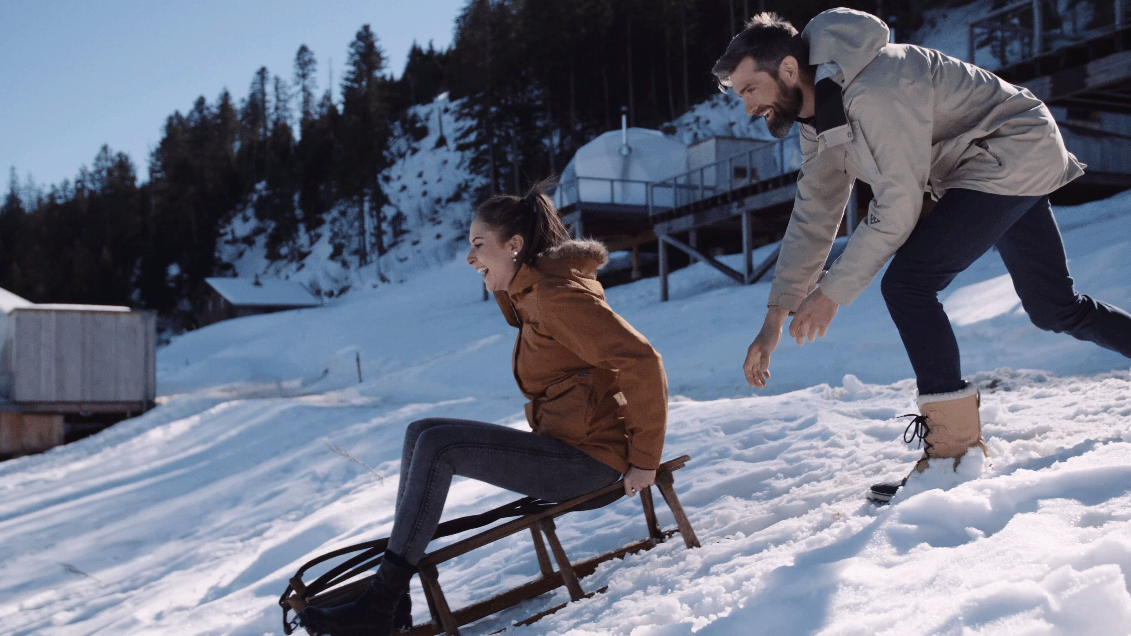 A snowy outdoor scene with a wooden sled and two people.