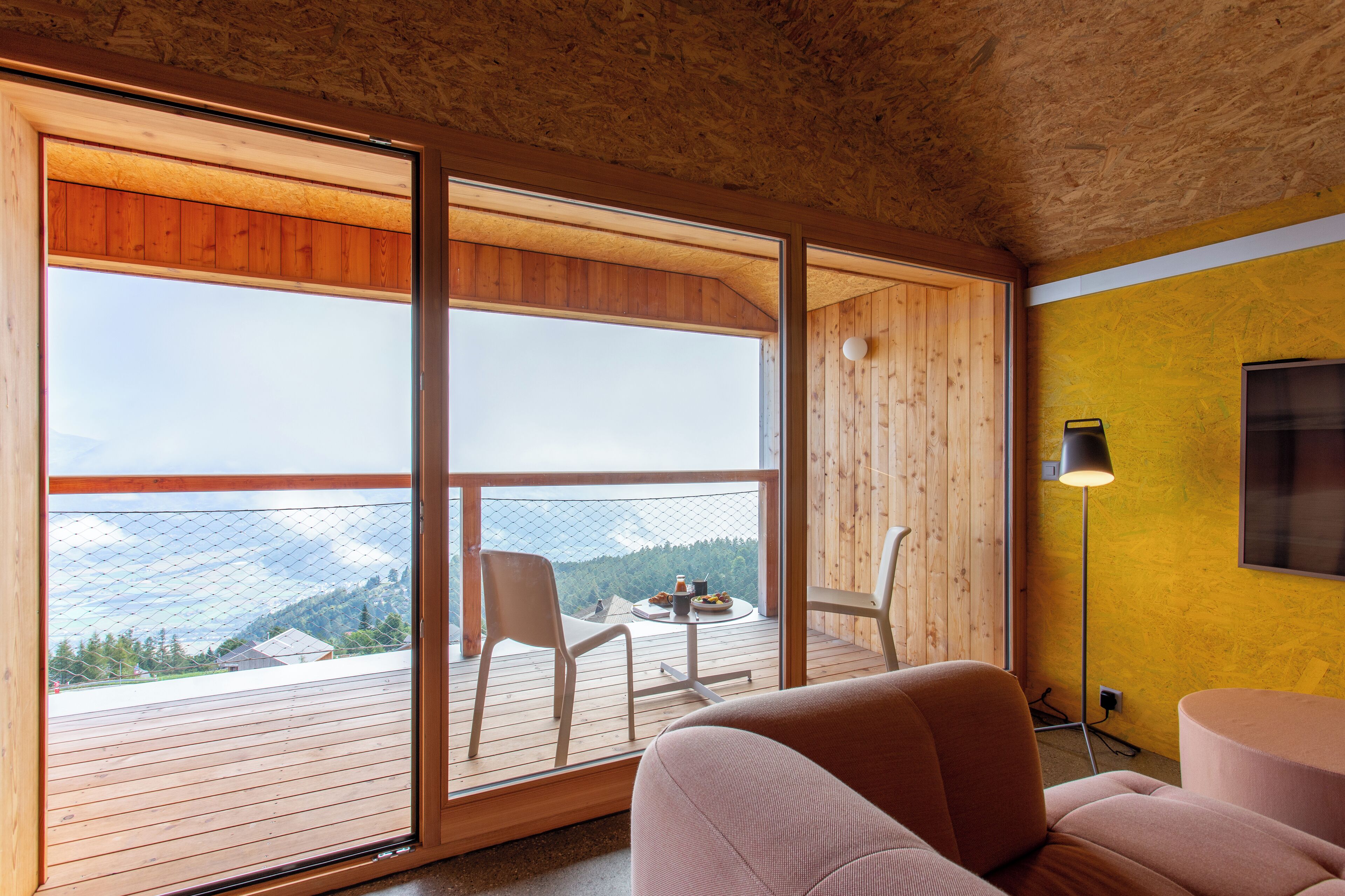 Una habitación con terraza de madera, balcón con mesa y sillas, y vistas a montañas.