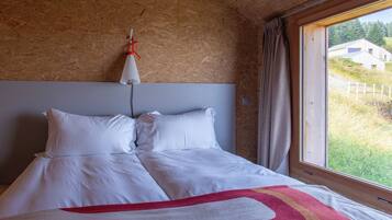 Een slaapkamer met een groot bed, een houten hoofdbord, een raam met uitzicht op een huis en bomen, en een gordijn.